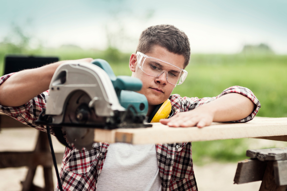 A young man cutting a plank with a saw and showing by example how crafting your dream home can be done.