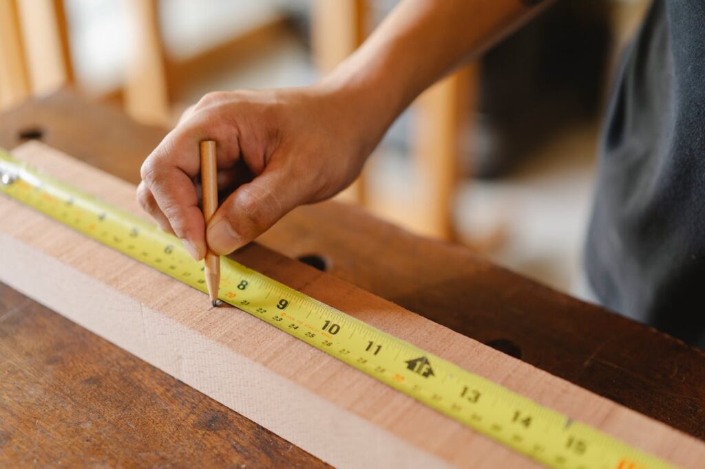 Man working with a yellow measuring tape on a wooden plank